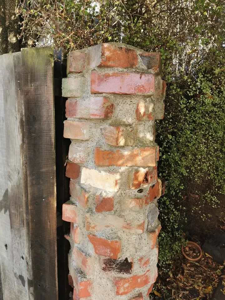 After: the same brick pillar with moss and algae removed, brick colours visible.