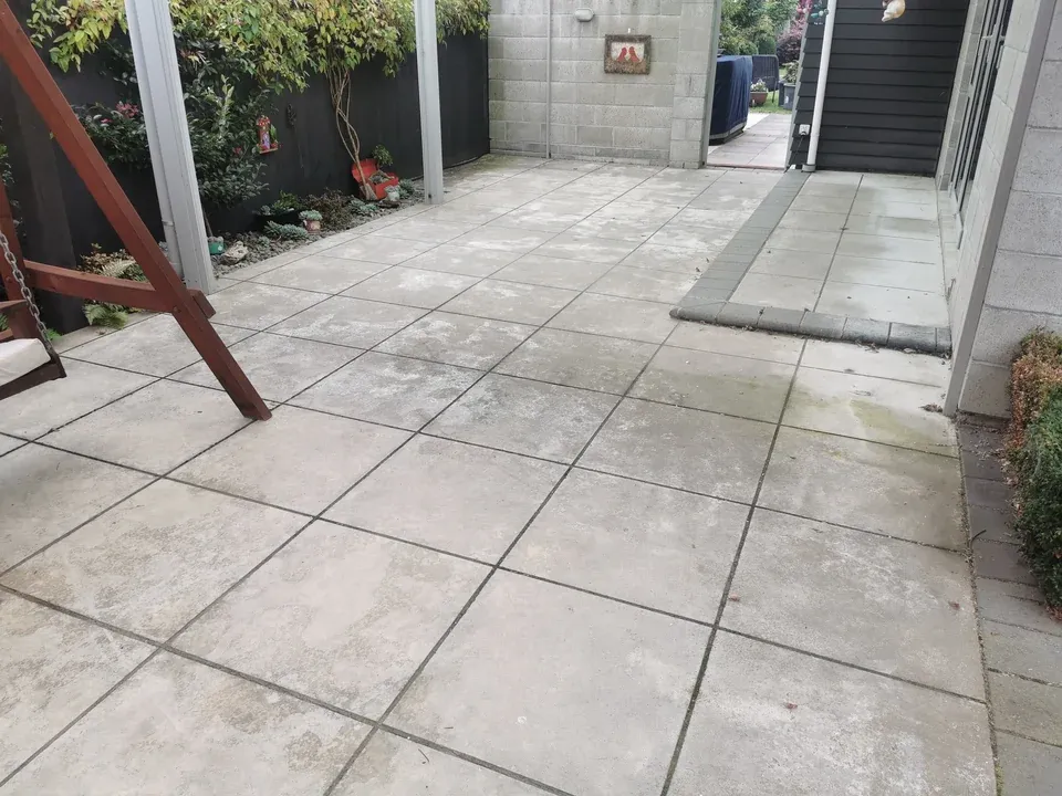 Before: large patio pavers with dark mottled staining and weathered grout lines.